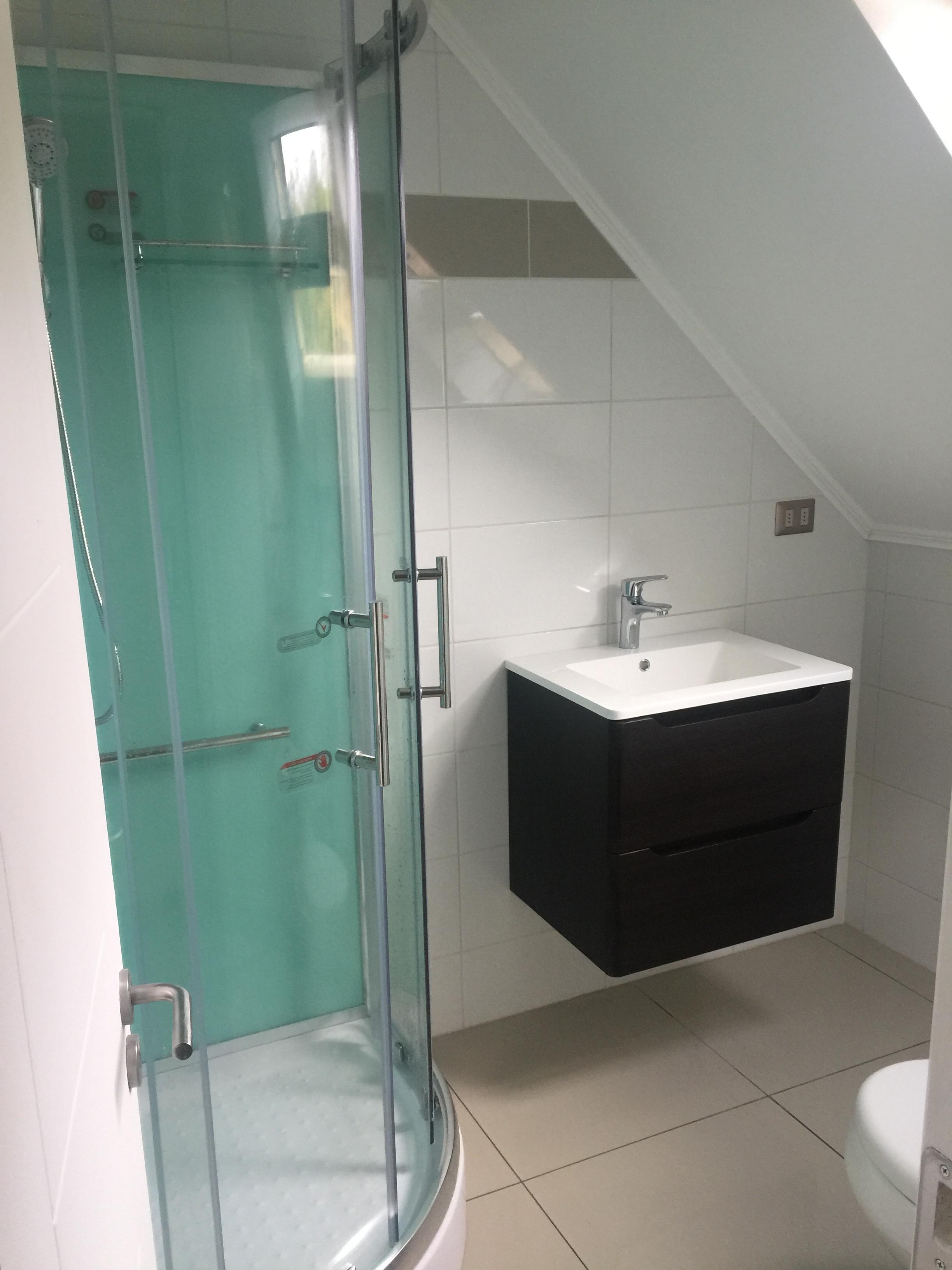Baño moderno terminado con vanitorio flotante de madera y ducha con mampara